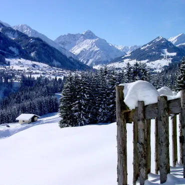 Easter Offer Snow-covered alpine landscape with wooden fence, trees, cabin, and mountain village in the background